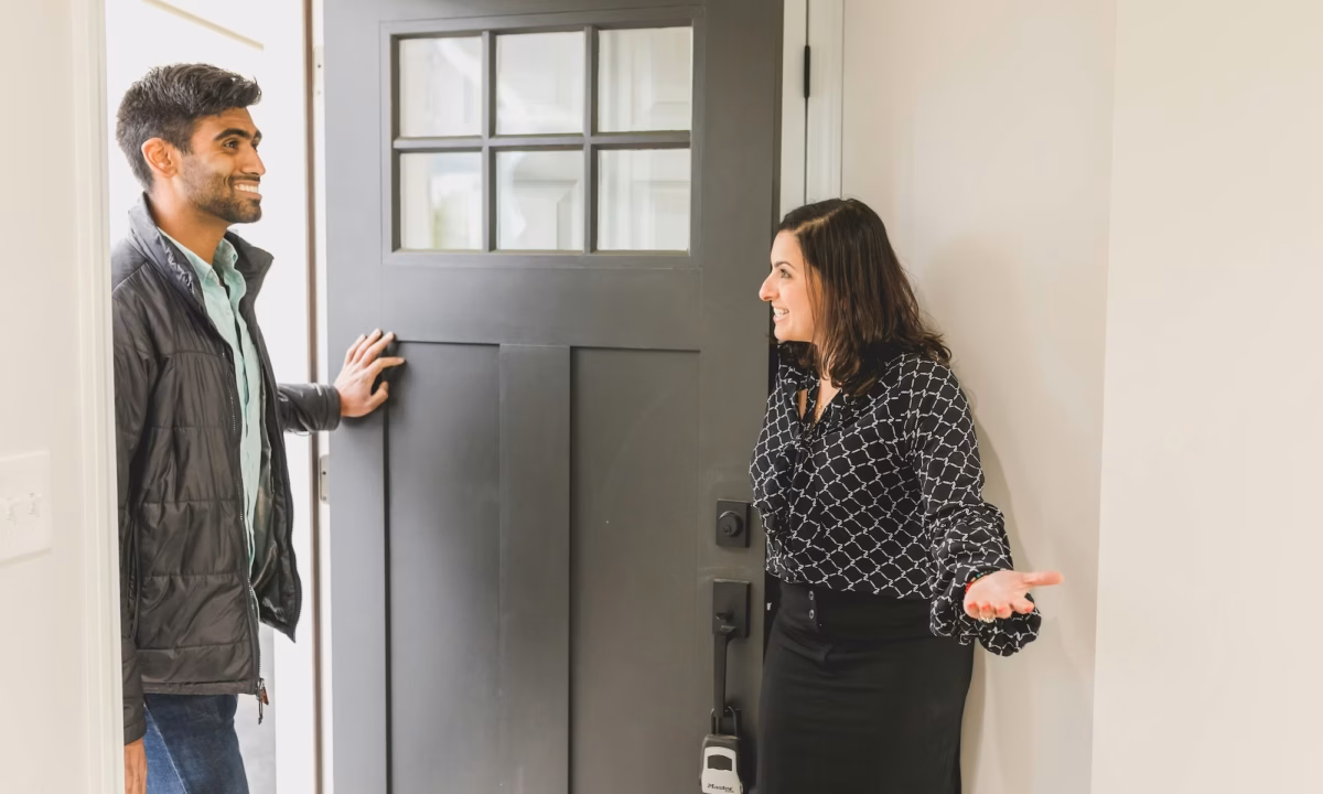 An agent opens the door to her real estate open house, greeting an attendee and potential homebuyer