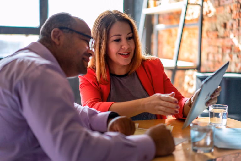 An agent sits with a client at a desk, showing him a real estate listing on her white-labeled mobile app