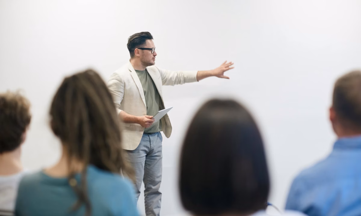 An instructor gestures on a white board in front of a class of students, illustrating how real estate coaches can help agents and brokers succeed.