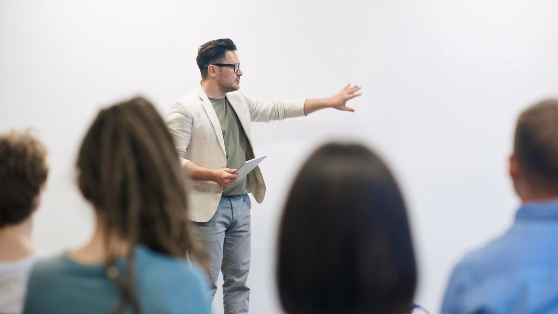 An instructor gestures on a white board in front of a class of students, illustrating how real estate coaches can help agents and brokers succeed.