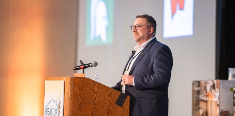 chris linsell stands onstage in front of a dais speaking at the Realtor Summit conference