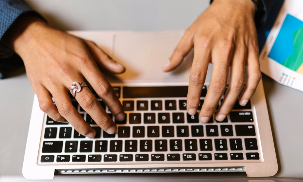 A real estate agent types on their laptop next to a printout of their email marketing strategy template