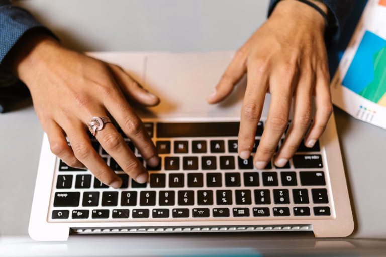 A real estate agent types on their laptop next to a printout of their email marketing strategy template