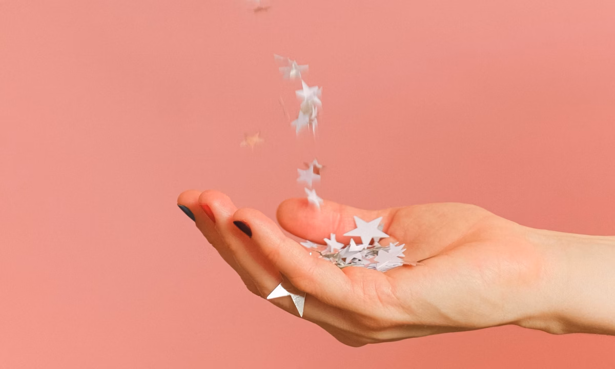A hand outstretched on a pink background catching stars as a symbol of how to ask clients for reviews