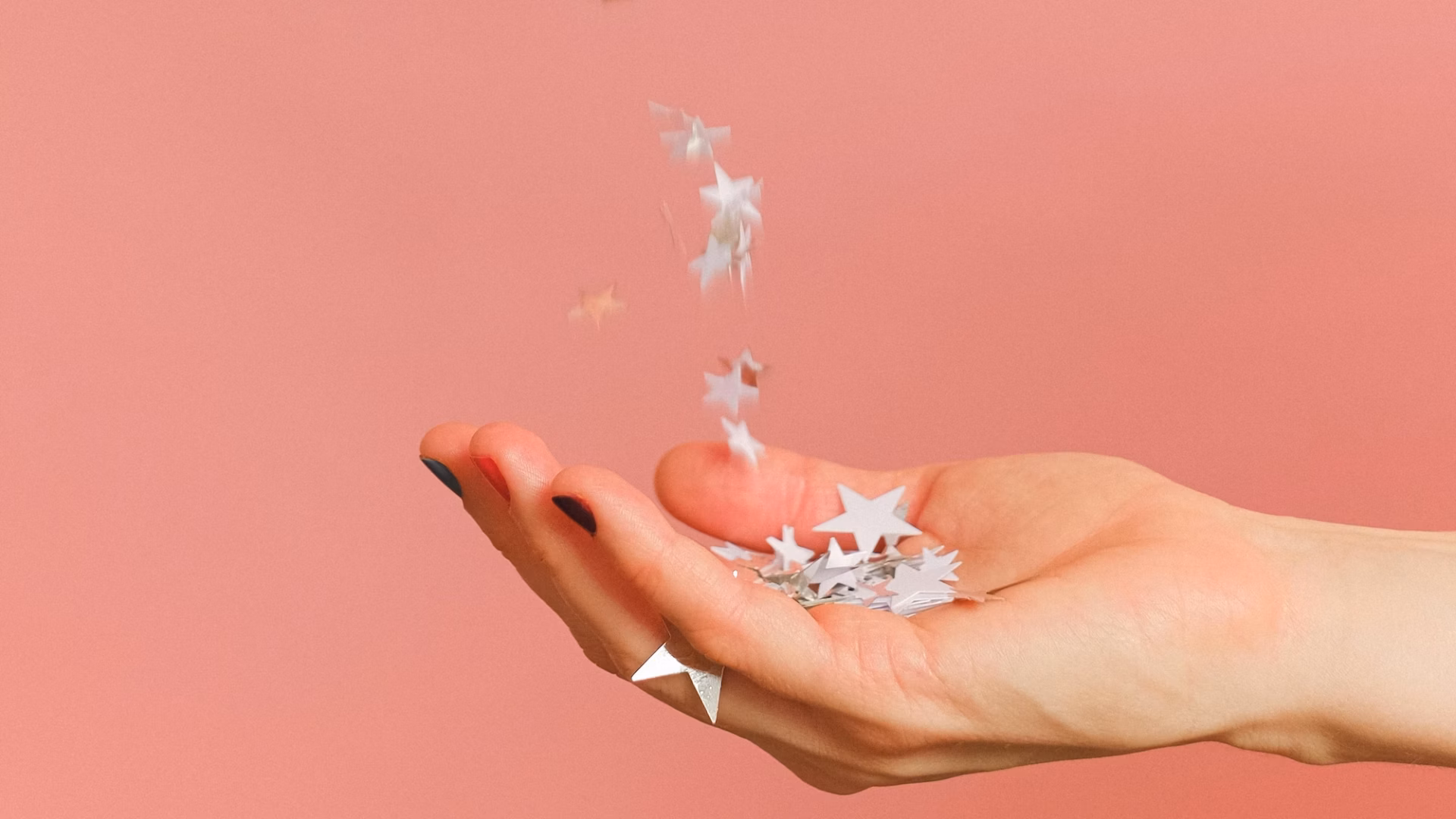 A hand outstretched on a pink background catching stars as a symbol of how to ask clients for reviews