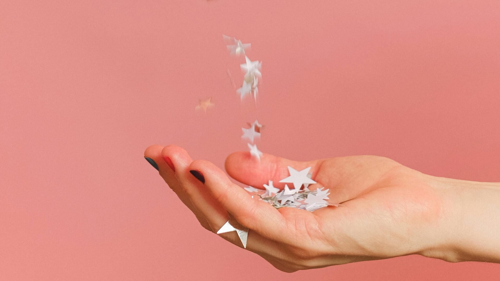 A hand outstretched on a pink background catching stars as a symbol of how to ask clients for reviews