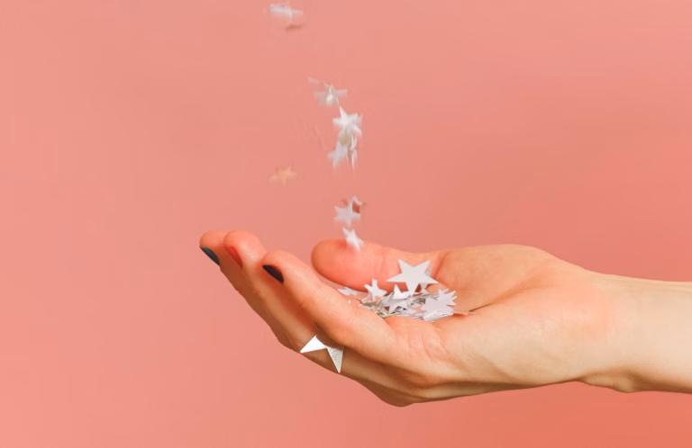 A hand outstretched on a pink background catching stars as a symbol of how to ask clients for reviews