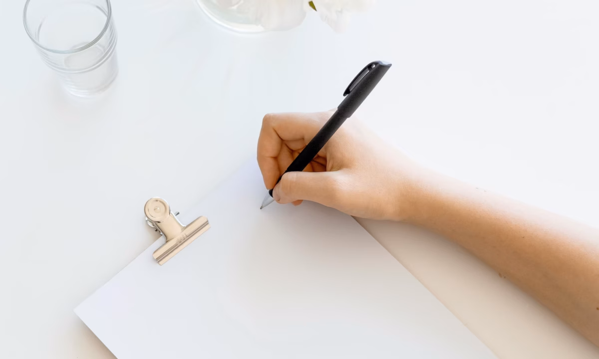 Real estate agent writing with a black pen on a white pad of paper, working on creating their personal brand statement