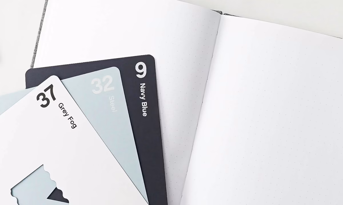Three color swatches are fanned out on top of a blank journal, representing a brainstorming session to come up with real estate branding ideas