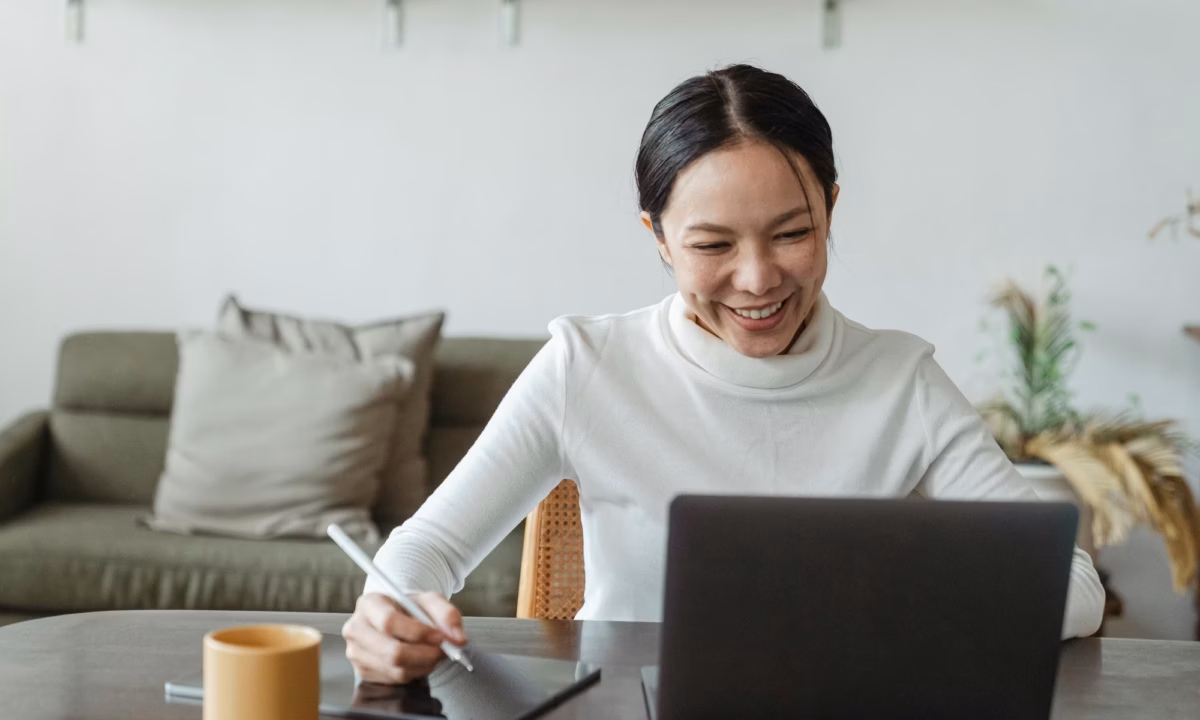 A real estate agent sits in front of a laptop smiling, jotting something down on her tablet about her Real Estate Marketing ROI with luxury presence