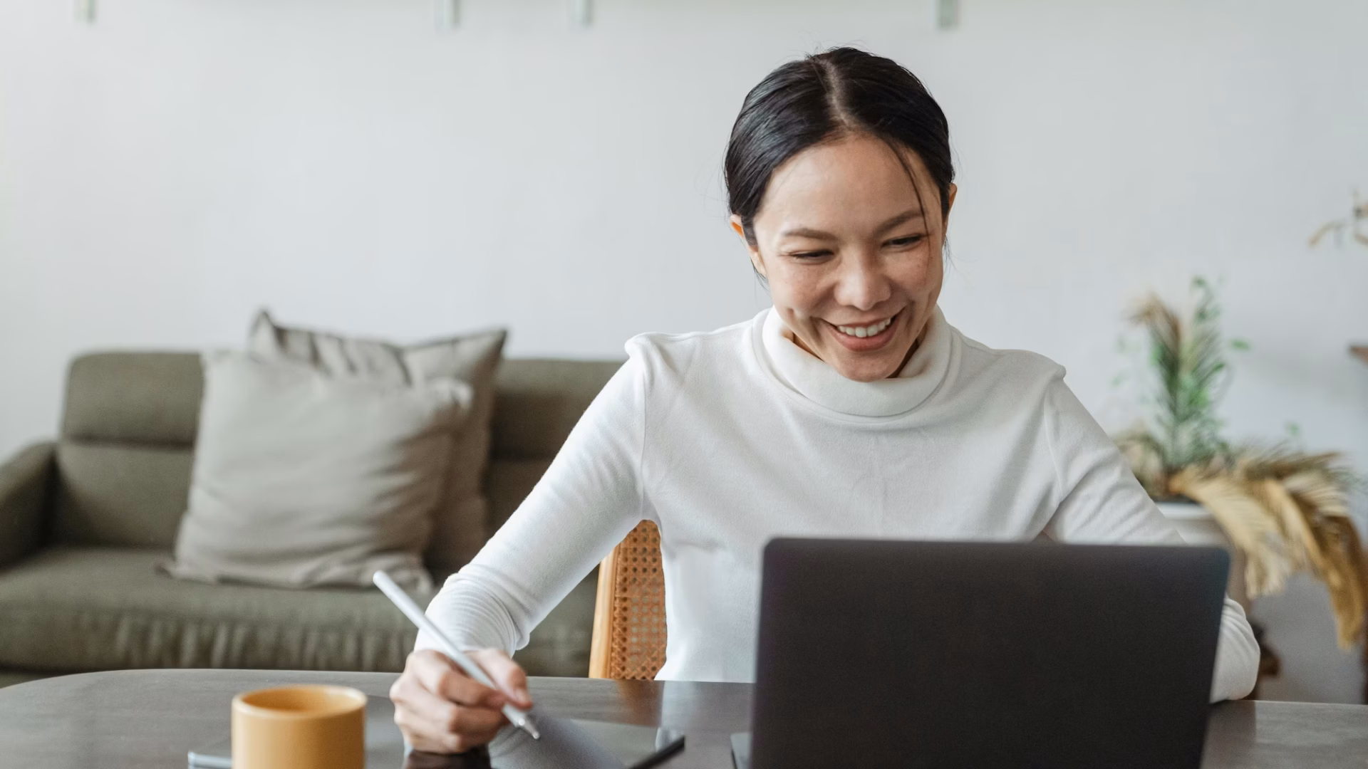 A real estate agent sits in front of a laptop smiling, jotting something down on her tablet about her Real Estate Marketing ROI with luxury presence