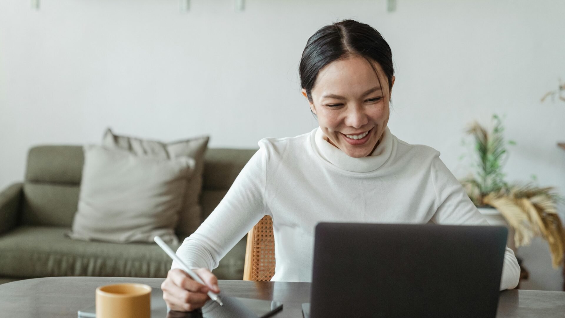 A real estate agent sits in front of a laptop smiling, jotting something down on her tablet about her Real Estate Marketing ROI with luxury presence