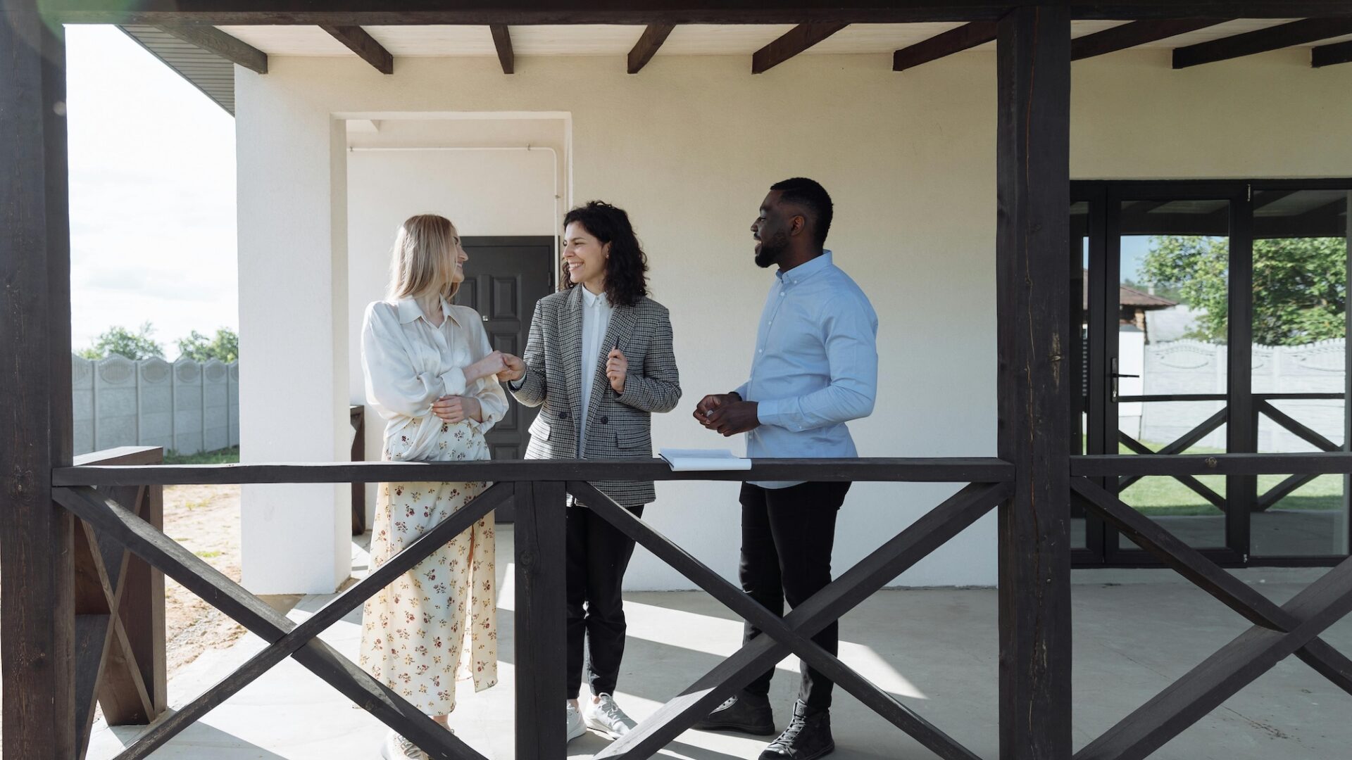 A real estate agent stands on a porch with two house hunters happy to have found her target audience in real estate