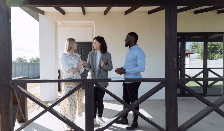 A real estate agent stands on a porch with two house hunters happy to have found her target audience in real estate