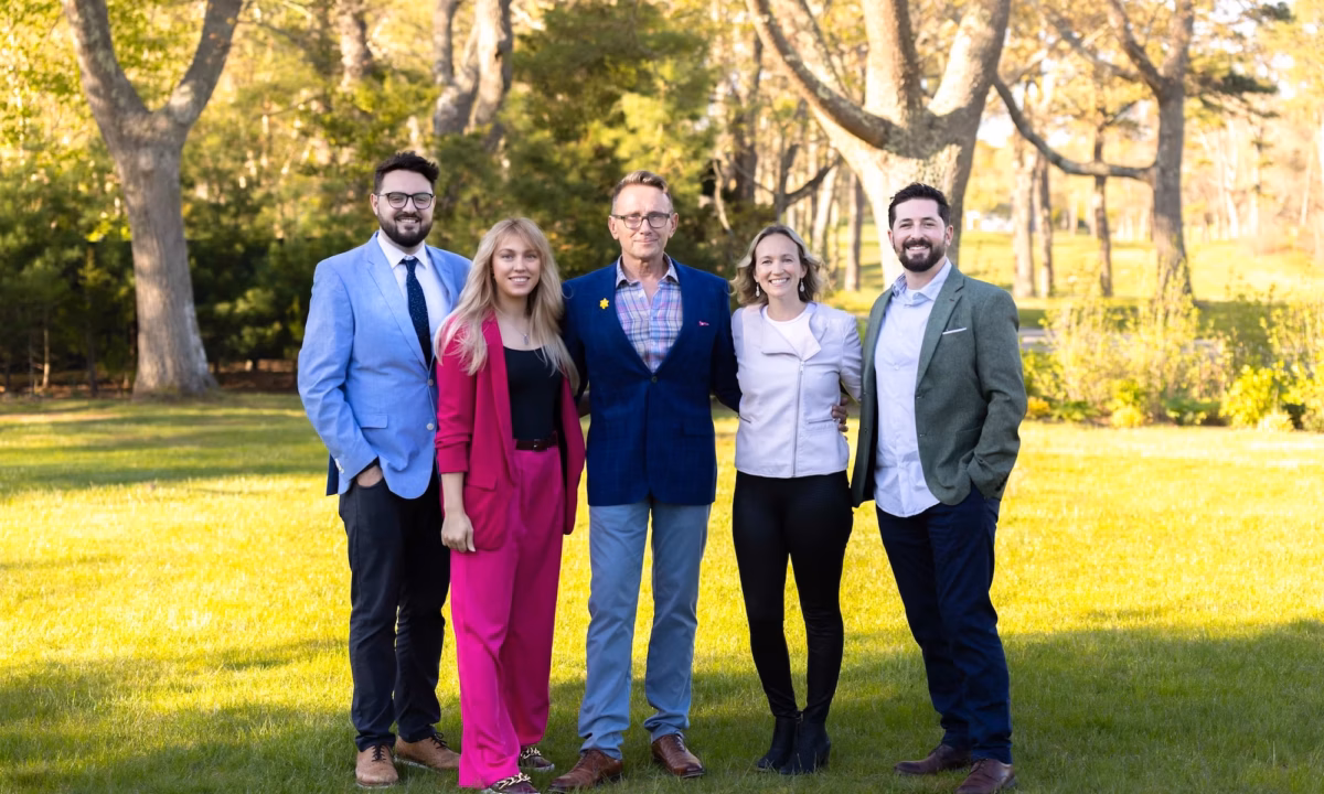 The guthrie schofield real estate team poses together on a green lawn in front of trees