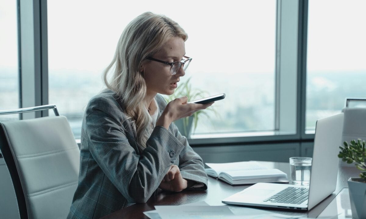 A real estate agent speaks into her phone at a desk, sending a message to her agentic AI marketing specialist