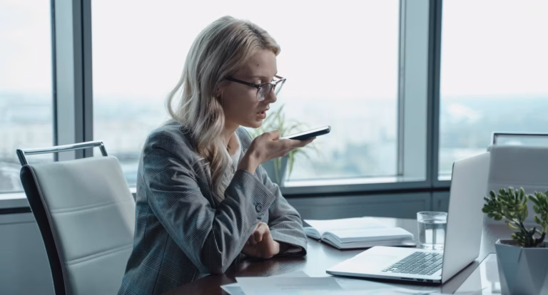 A real estate agent speaks into her phone at a desk, sending a message to her agentic AI marketing specialist