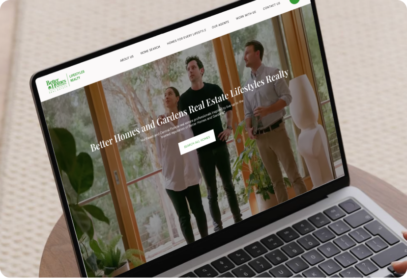 A laptop sits on an ottoman, screen open to Better Homes and Gardens Real Estate Lifestyles Realty’s website created by Luxury Presence