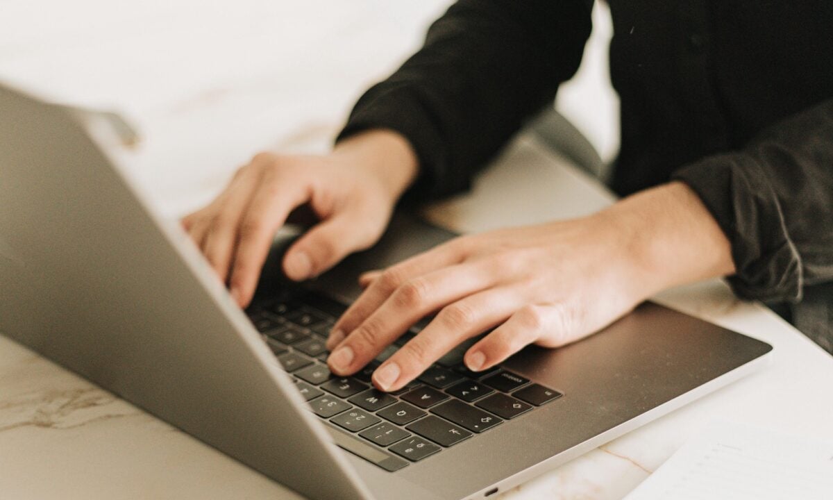 real estate agent sits at a laptop on a white desk trying to choose between the Real Estate Website Builders