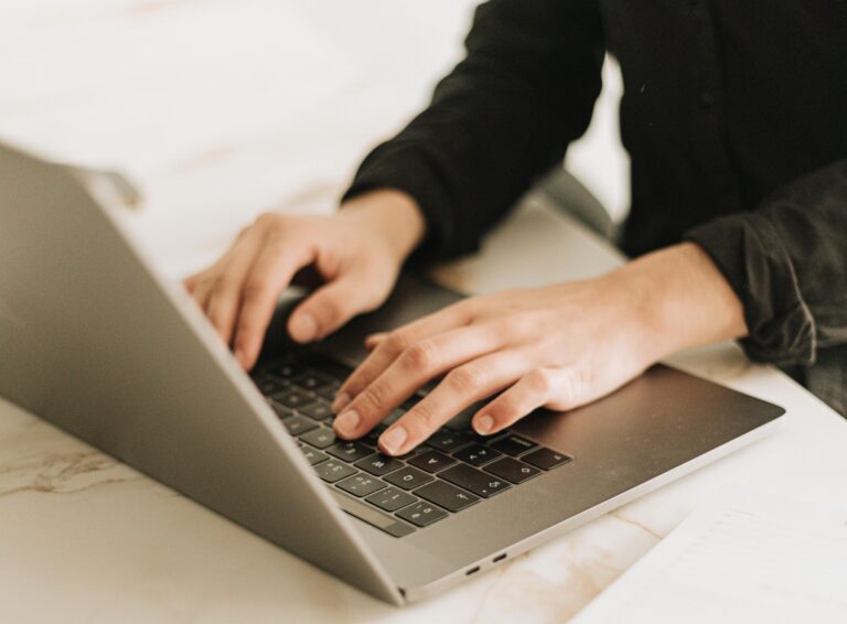 real estate agent sits at a laptop on a white desk trying to choose between the Real Estate Website Builders