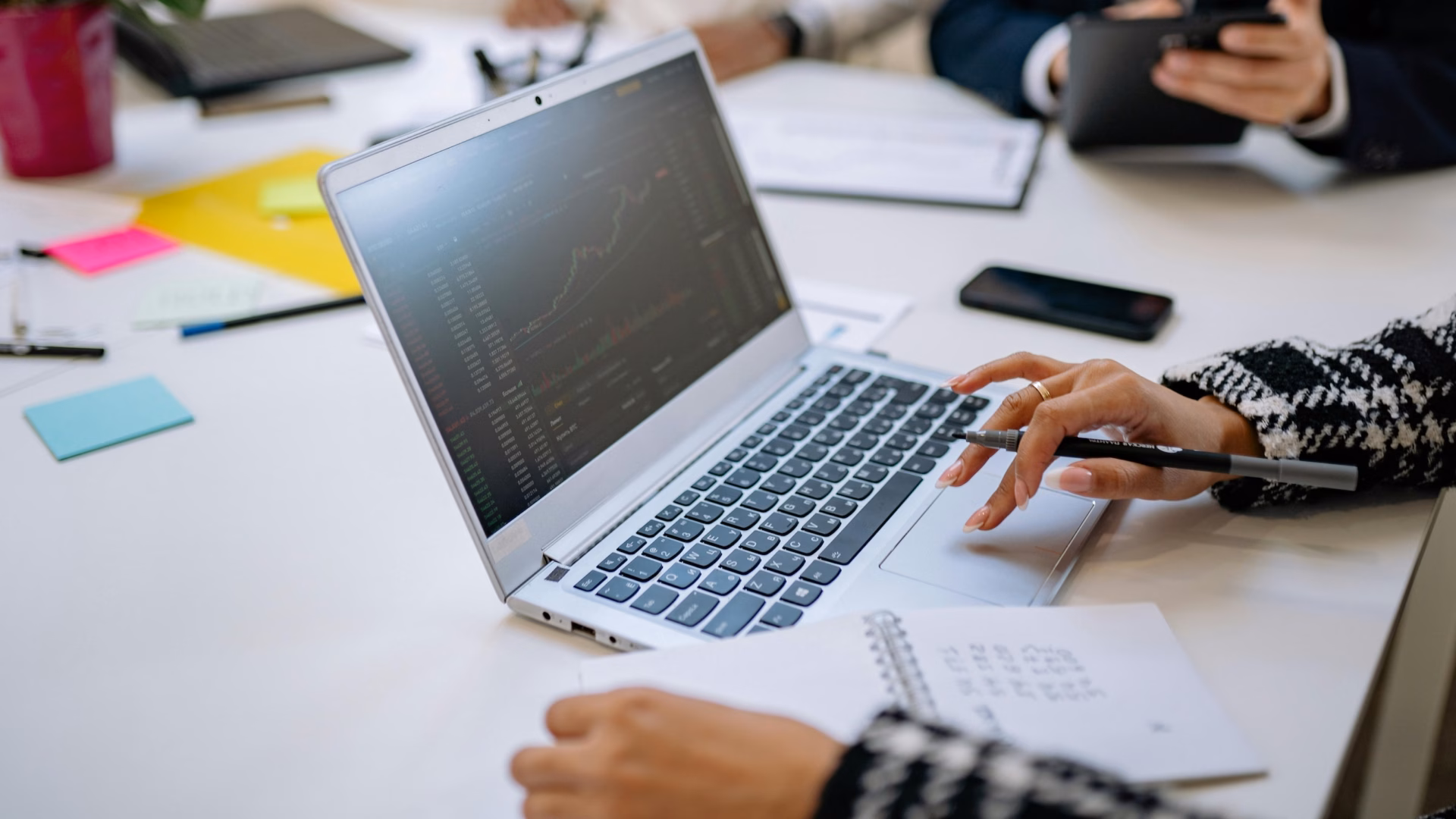 One real estate agent sits in front of a laptop screen showing website analytics with another agent behind her, discussing the pros and cons of Luxury Presence vs. BoomTown