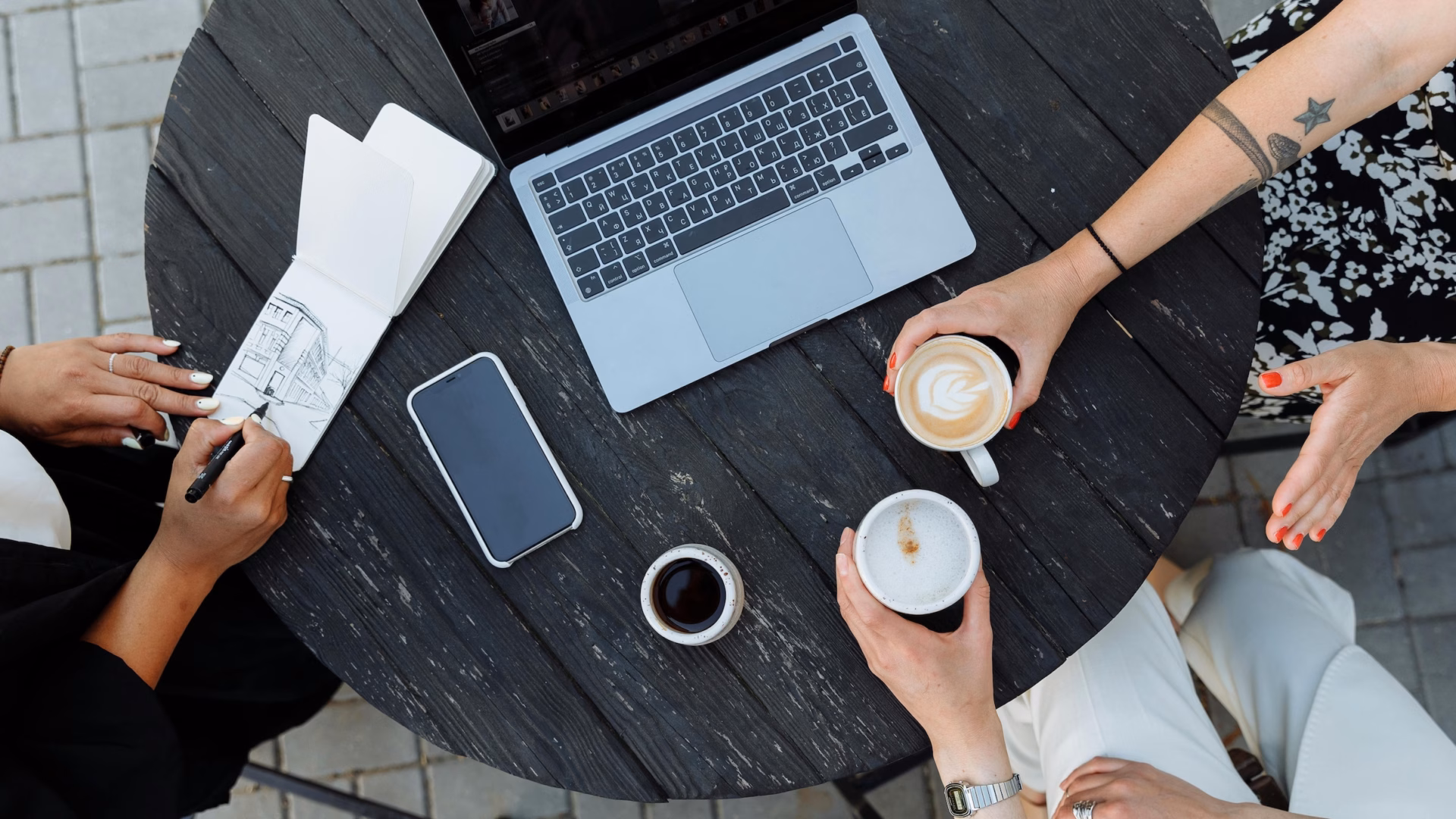 Three real estate agents sit at a cafe table having coffee around a laptop, discussing the choice between Luxury Presence vs. Ylopo