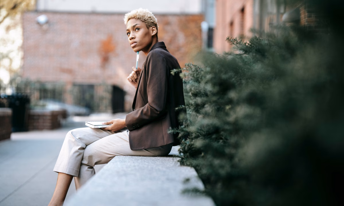 A real estate agent sits on a concrete bench outside with a pencil up against her chin, trying to decide between luxury presence vs. boomtown