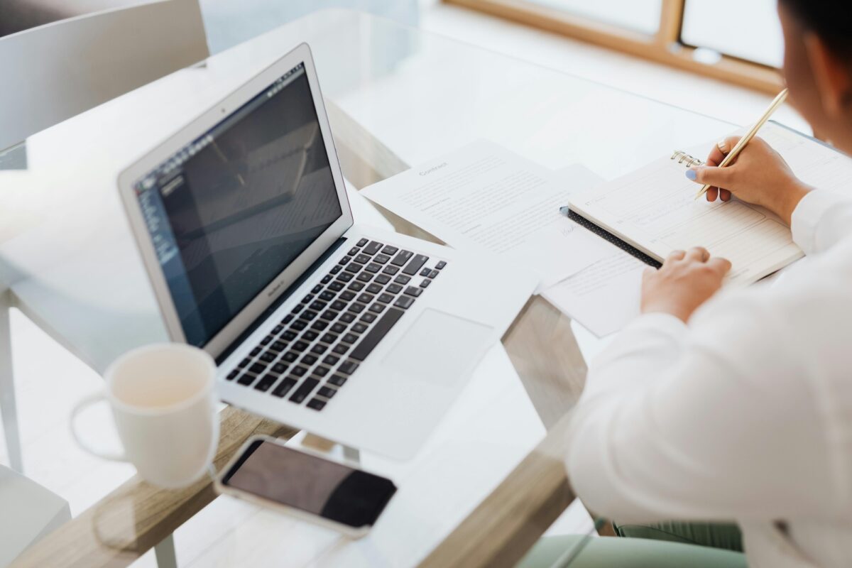Real estate agent sitting at a desk in front of a laptop and cup of coffee, writing down pros and cons of Luxury Presence vs. Agentfire