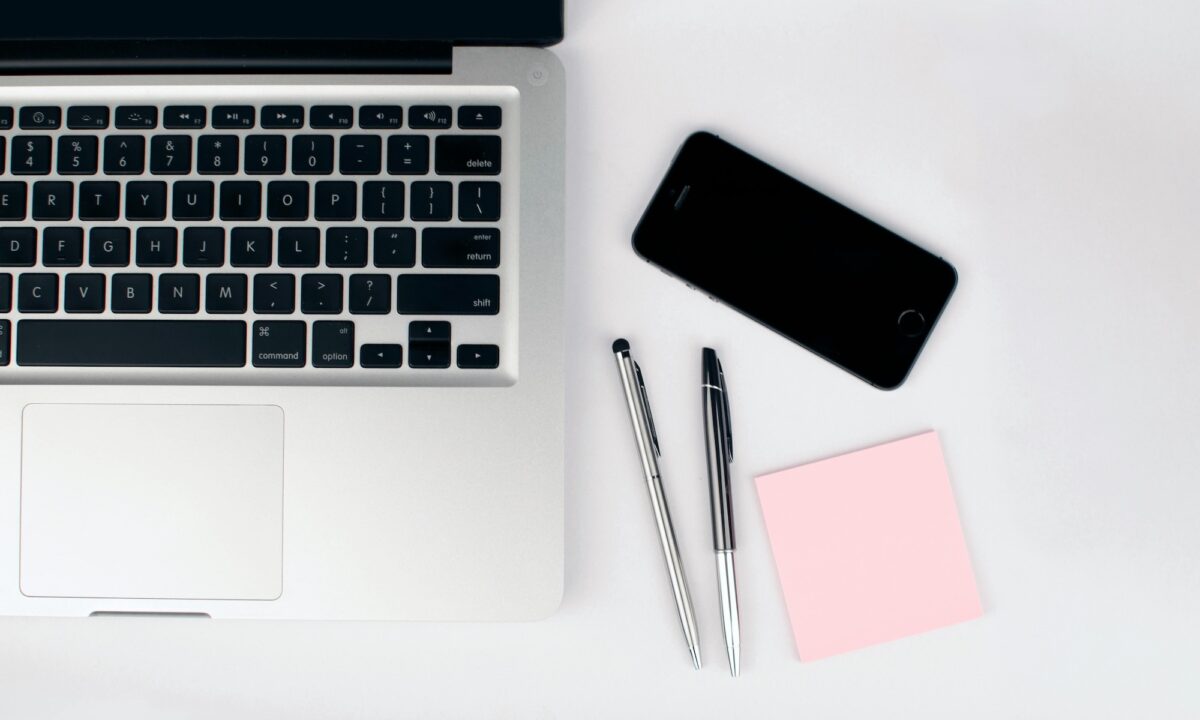 A laptop, two pens, a smart phone sit on a white desk